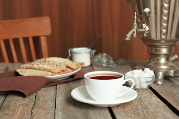 Vintage samovar, cup of hot drink and pancakes served on wooden table. Traditional Russian tea ceremony
