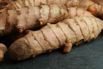 Many raw turmeric roots on black textured table, closeup