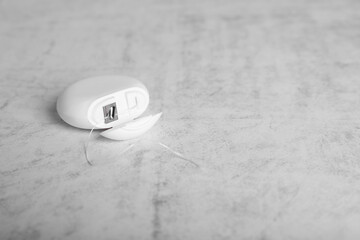 Container with dental floss on light grey textured table. Space for text