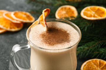 Glass cup of delicious eggnog with dried orange slice and cinnamon on gray table, closeup