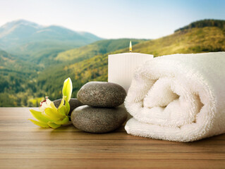 Fresh towel, spa stones and exotic flower on wooden table against beautiful mountain landscape