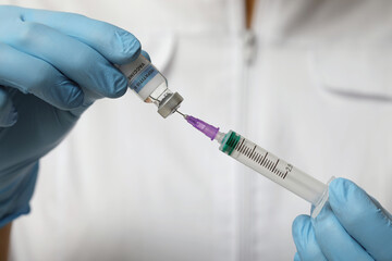 Doctor filling syringe with hepatitis vaccine from glass vial, closeup