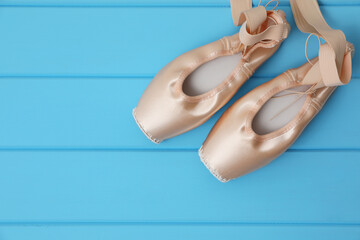Beautiful beige ballet shoes with cute ribbons on light blue wooden table, top view. Space for text