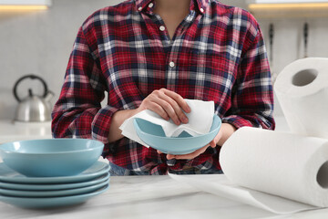 Woman wiping bowl with paper towel at white marble table in kitchen, closeup