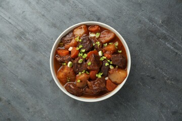 Delicious beef stew with carrots, green onions and potatoes on grey table, top view