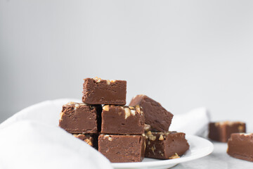 chocolate fudge with nuts on a white ceramic plate, chocolate fudge cut into pieces, fudge candy on a plate