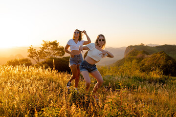 Happy female friends having fun outdoors with sunset and mountains in the background.