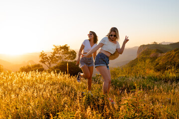 Happy female friends having fun outdoors with sunset and mountains in the background.