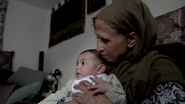 Bangladeshi Grandmother Looking Affectionately At Her Grandson Who Is Watching TV In Living Room. Low Angle, Slow Motion