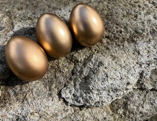 Three golden eggs on grey rock