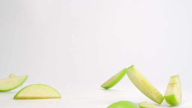 Cut up green apple slices landing on white table top and bouncing in all directions in slow motion