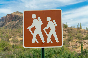 Hiking trail sign with two white stick figures on walk with brown pain square shape for park or...