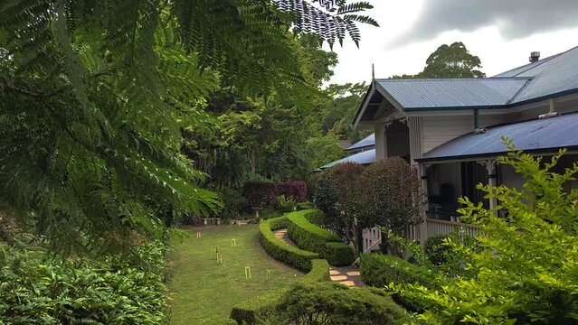 Smooth cinematic descending reveal shot of a classic traditional country Queenslander house, nestling in neatly manicured landscaped garden