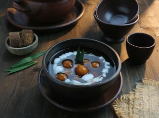 serving a bowl of starch balls with brown sugar sauce and coconut milk on a wooden table