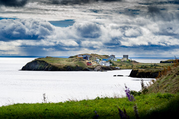 Scenic landscape of small east coast homes on a peninsula overlooking high cliffs along the Atlantic Ocean near Port Rexton Newfoundland.