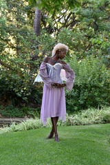 Portrait of beautiful African woman wearing purple fantasy costume, magical fairy wings and flower crown afro, wandering around forest location with natural lighting.