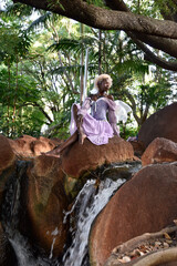 Portrait of beautiful African woman wearing purple fantasy costume, magical fairy wings and flower crown afro, wandering around forest location with natural lighting.