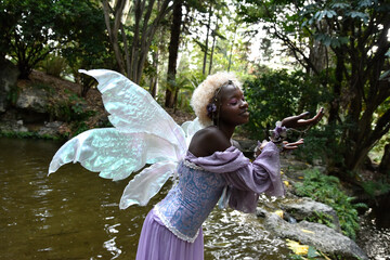 Portrait of beautiful African woman wearing purple fantasy costume, magical fairy wings and flower...