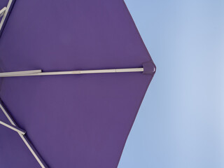 Purple beach umbrella. Blue sky in the background. View from below. Relaxing context. Summer holidays by the sea. General contest and location