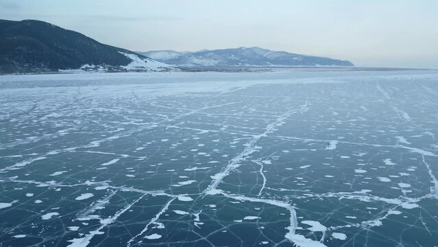 Winter drone flight over the clear ice of Lake Baikal near the mountain coast. Traveling and discovering the wonders of nature