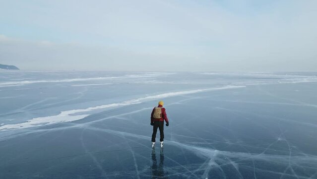 A man in a red jacket with a backpack is skating on the blue transparent ice of the endless lake Baikal. Unique places of the earth