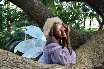 Portrait of beautiful African woman wearing purple fantasy costume, magical fairy wings & flower...