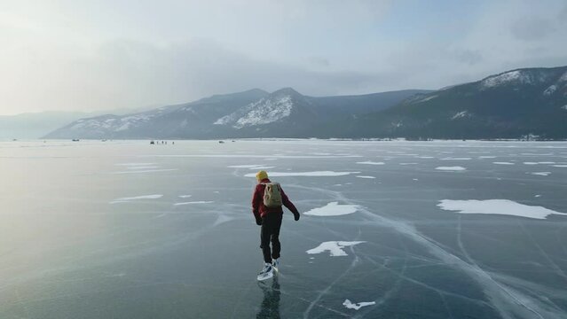 A man in a red jacket with a backpack is skating on the blue transparent ice of the endless lake Baikal. Unique places of the earth
