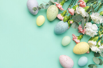 Easter colored eggs and a bouquet of white and pink carnations with eucalyptus branches on a soft green background.