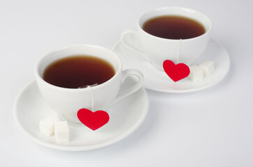 Two white cups of tea on saucers with two red heart labels. White background.	