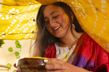 close up of a young woman with gulal on her face holding gulal bowl
