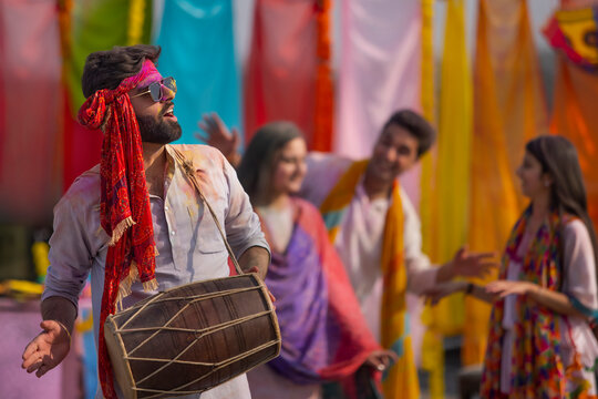A group of young men and women happily dancng together while celebrating holi