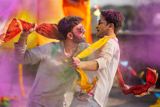 two young indian men with colored face dancing together during holi color festival