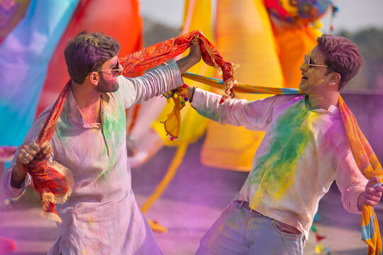 two young indian men with colored face dancing during holi color festival