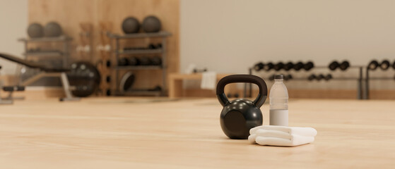 A kettle bell, towels and a bottle of water on a wooden gym floor in modern fitness center.