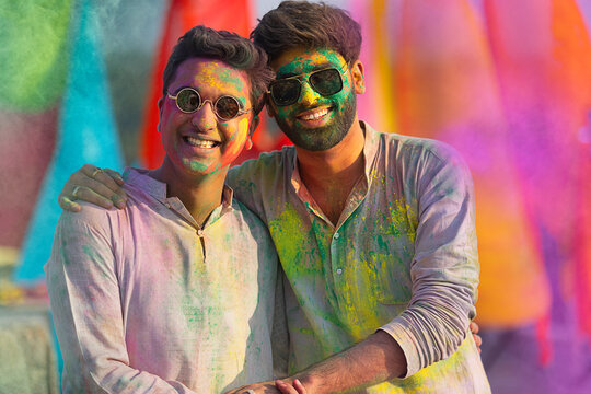 close-up portrait of smiling young men with colourful face and sunglass on holi