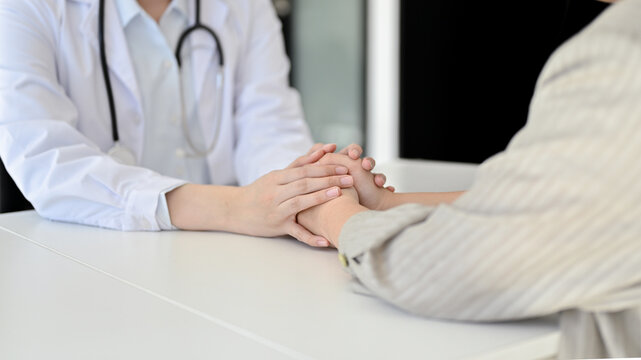 Close-up image of a caring female doctor holding a patient's hands to reassure and comfort her