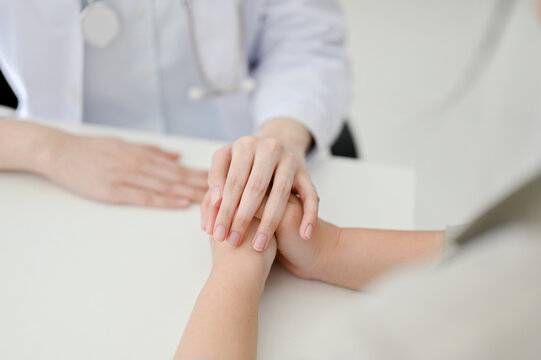 Close-up image of a caring female doctor holding a patient's hands during the meeting.