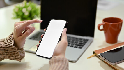 A businesswoman working from home, using her smartphone at her working desk.