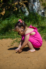 Fototapeta premium A little girl in a pink dress is playing on the sand. A child walks along the coast.