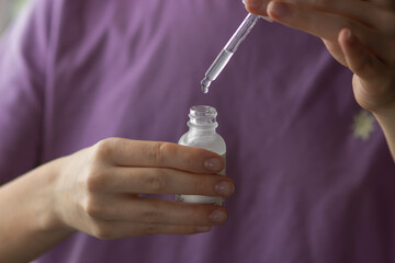 Woman hand holds pipette over glass bottle with facial vitamin serum or essential oil. Concept of skincare and face care