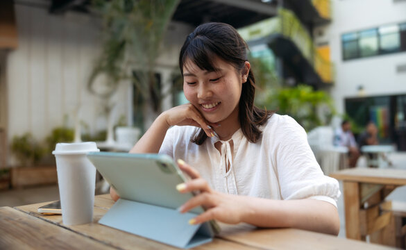 Young asian girl with freckles smiling and studying online with a tablet