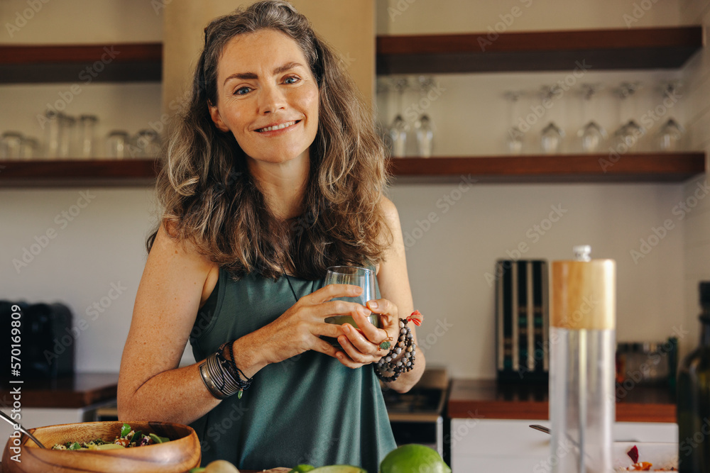 Wall mural vegan senior woman smiling while holding a glass of green juice