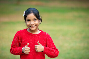 Indian little girl showing thumps up at park.