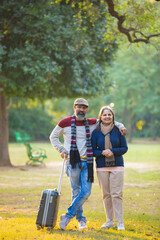 Indian Senior couple with travel bag at park.