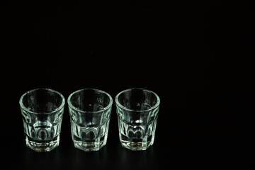 Empty shot glasses lined up against negative space black background waiting to be filled and...