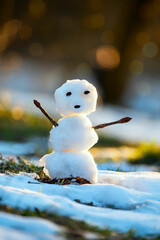 A small melting snowman in a clearing with melting snow and sun spots. The coming of spring. Warming.