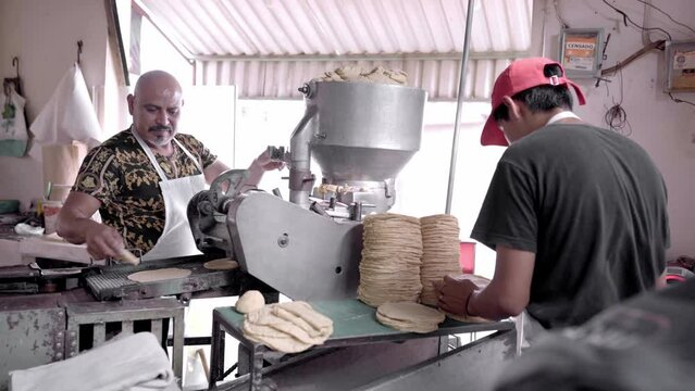 An adult man is working with his son producing corn tortillas with a nixtamall mill