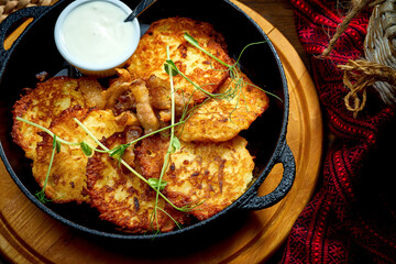 Traditional Ukrainian deruny with sour cream in a black pan. Ukrainian cuisine Potato pancake. Close up