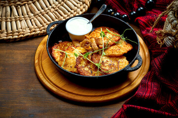 Traditional Ukrainian deruny with sour cream in a black pan. Ukrainian cuisine Potato pancake. Close up