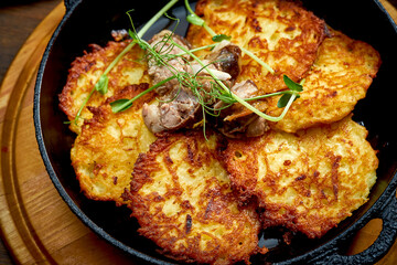 Traditional Ukrainian deruny with meat in a black pan. Ukrainian cuisine Potato pancake. Close up